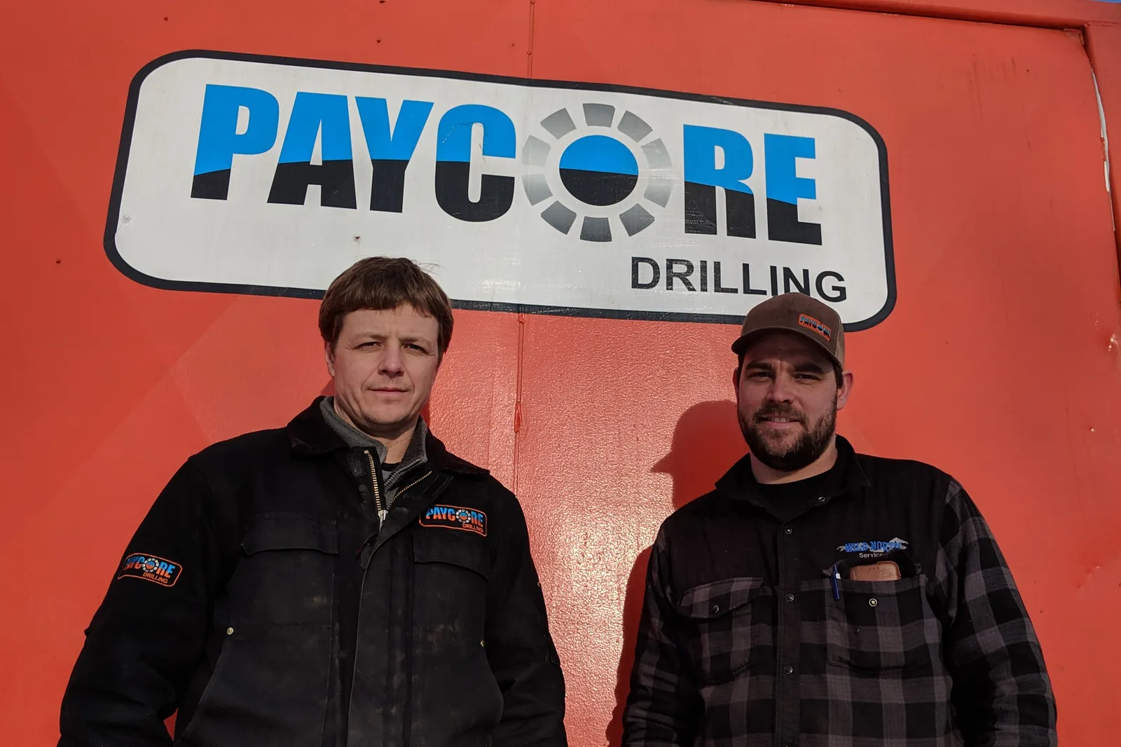 Two crew members in front of a Paycore Drilling sign
